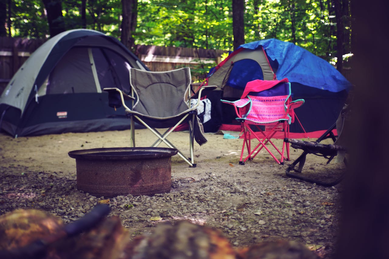 mobile-01 A serene campsite in the woods with colorful tents, camping chairs, and a fire pit, perfect for a leisure getaway.