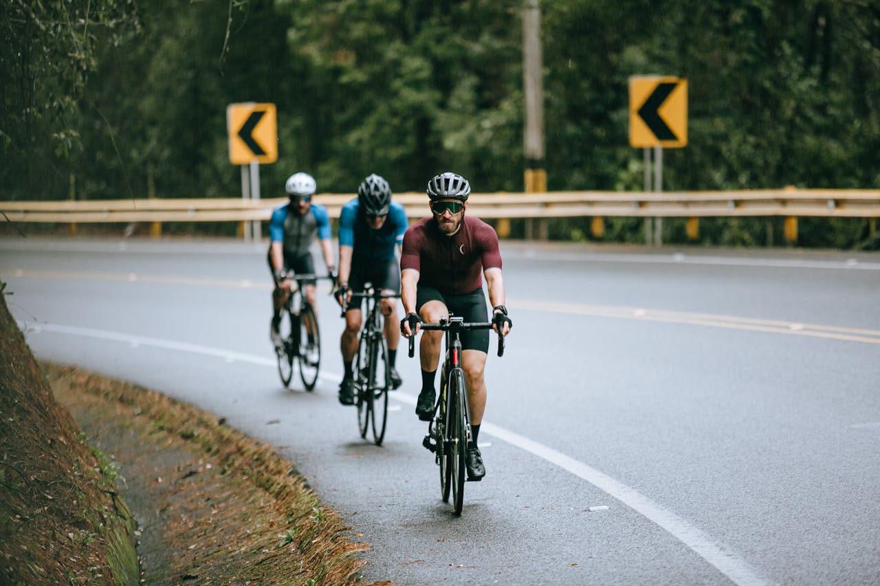 creative-03 Anonymous male cyclists in sportswear and helmets riding bicycles on fenced asphalt roadway in summer