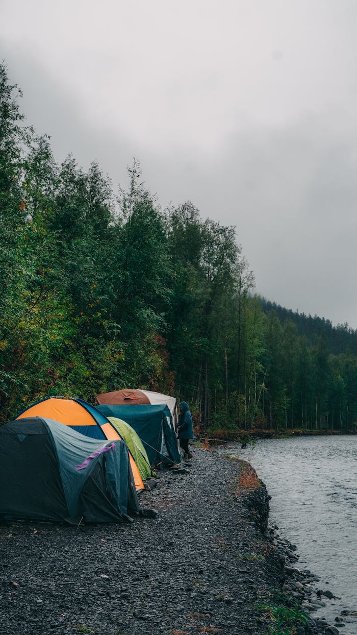brand-01 Vibrant tents set up by a tranquil riverside surrounded by lush forests.