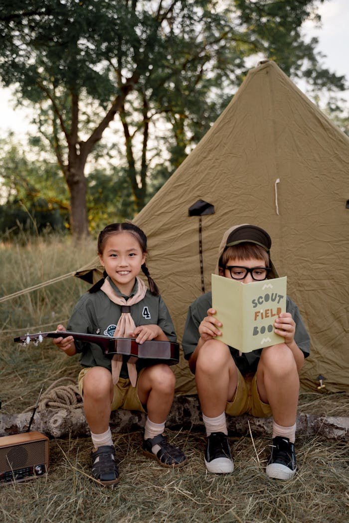 brand-02 Children enjoying a scouting camp, reading and playing ukulele beside a tent.